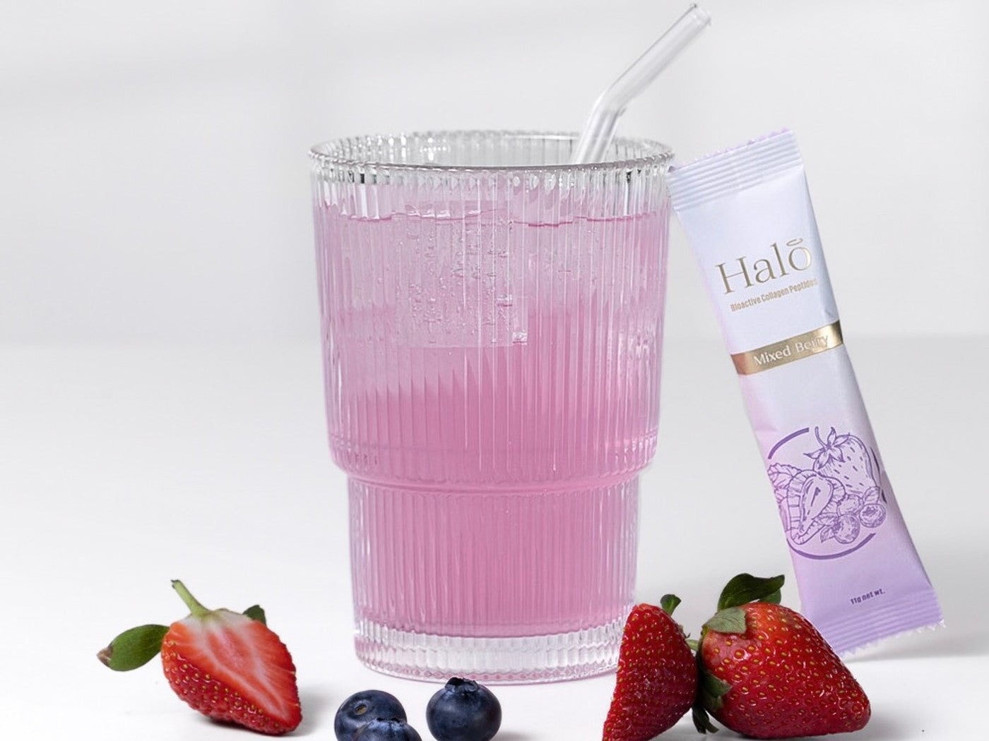 A Halo Mixed Berry sachet beside a pink drink with strawberries and blueberries
