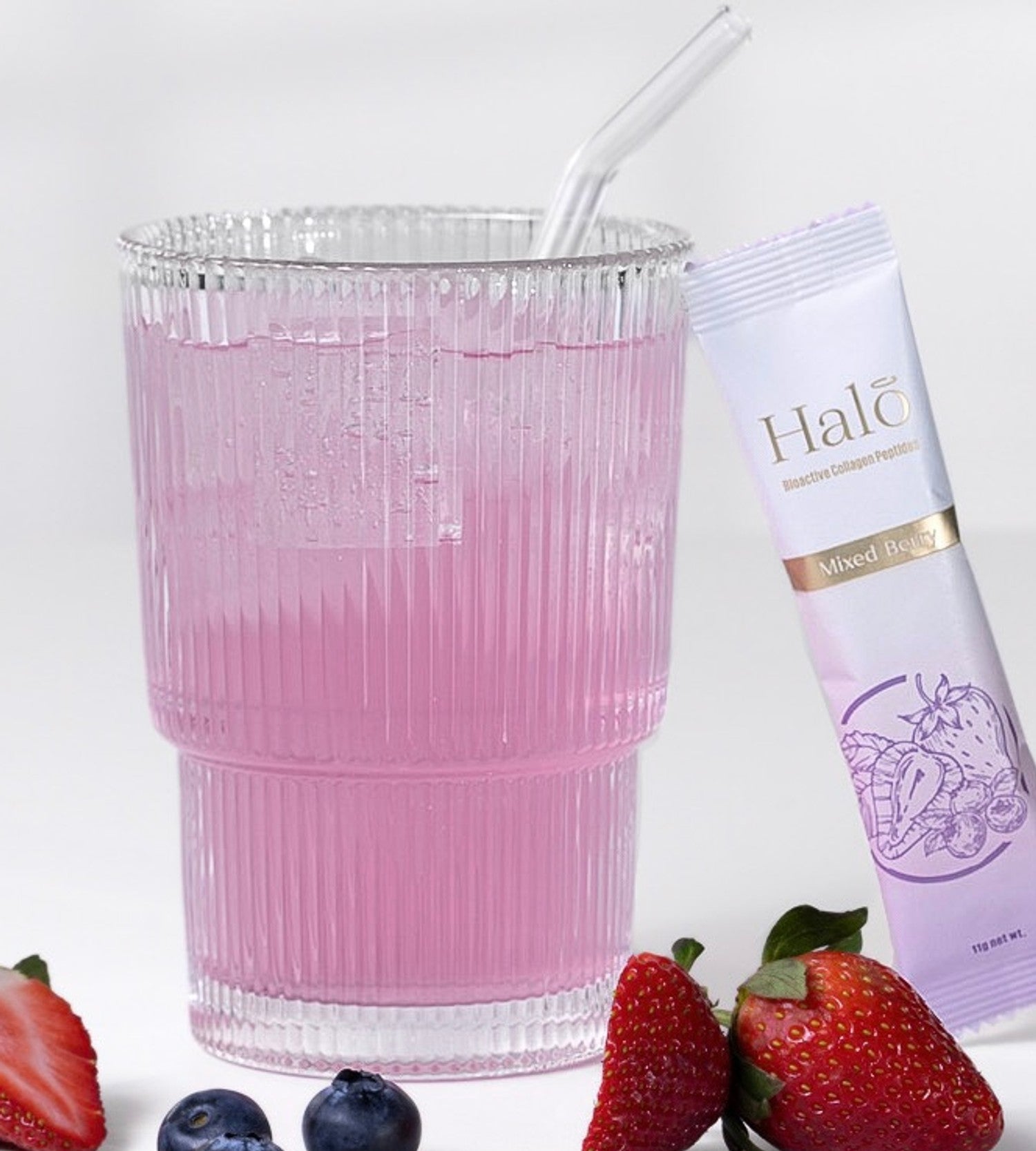 A Halo Mixed Berry sachet beside a pink drink with strawberries and blueberries