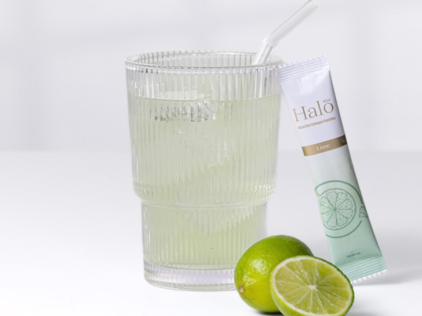 A Halo Lime sachet beside a glass of iced lime and fresh limes