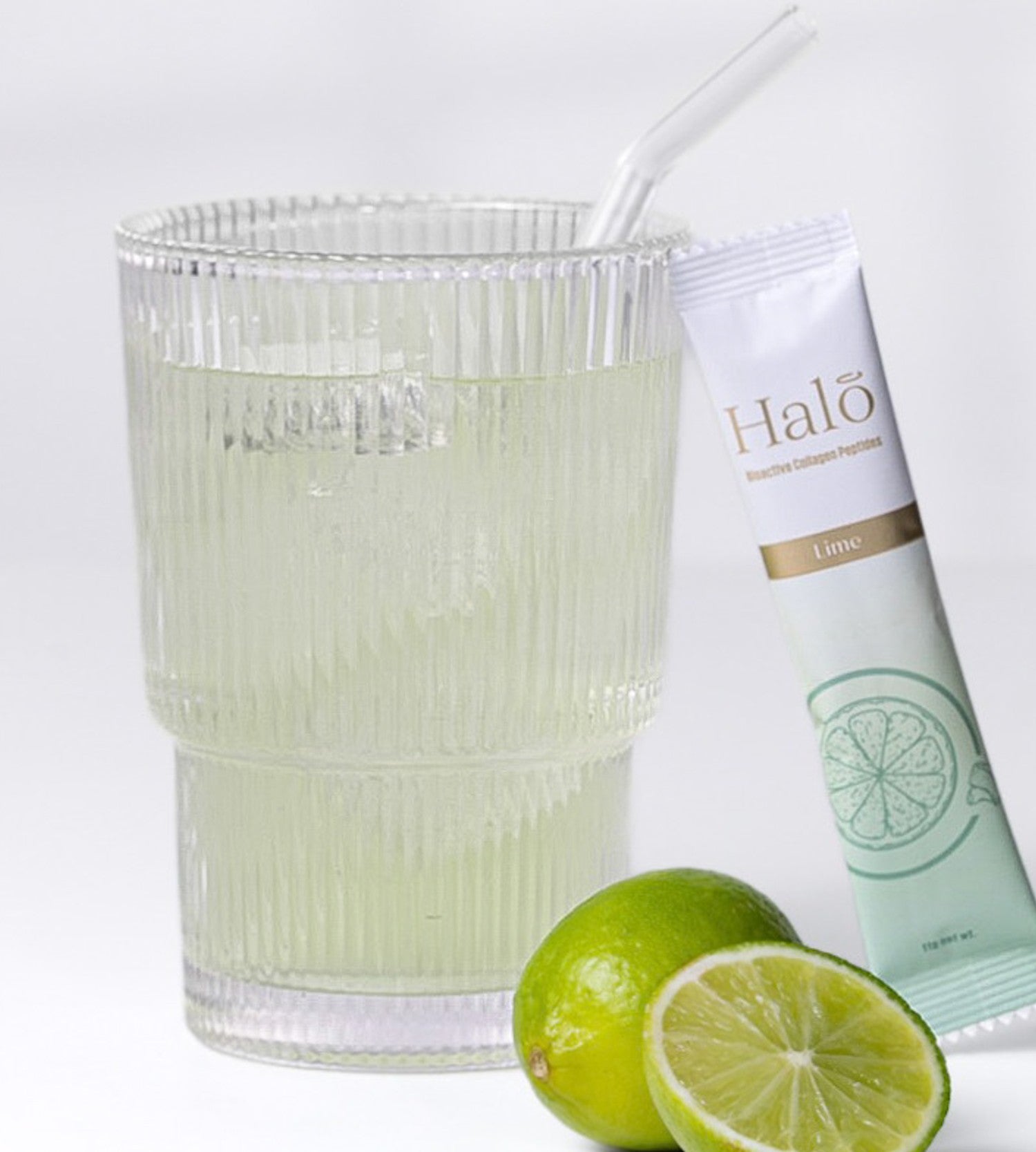 A Halo Lime sachet beside a glass of iced lime and fresh limes